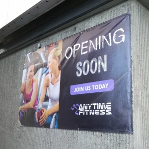 large banner for a gym that says opening soon installed on the side of a building