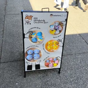 A sandwich board sign for an asian themed snack cafe on a busy sidewalk