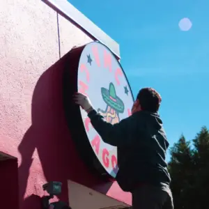 Man installing a round lightbox sign on a red wall in bright daylight